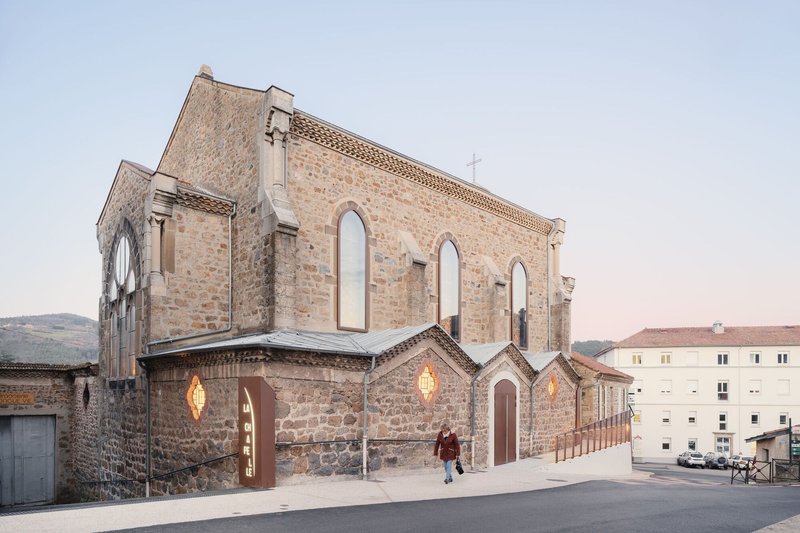 Stone church facade with empty arched windows and illuminated chapels attached at dusk