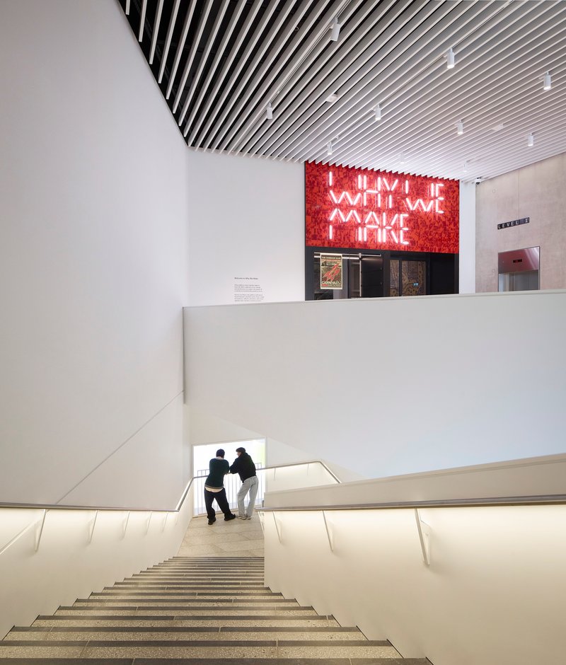 Wide staircase with integrated lighting and two visitors ascending toward the red neon installation above