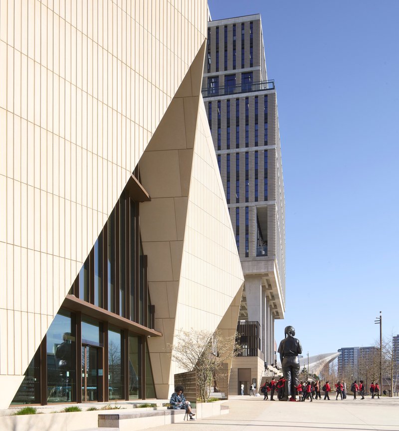 Public plaza with bronze sculpture and visitors in front of the angular entrance volume