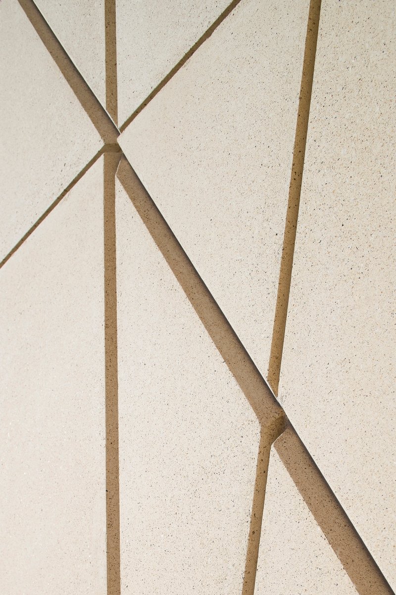 Detail of pale facade surface with brass or bronze inlay forming triangular geometric pattern