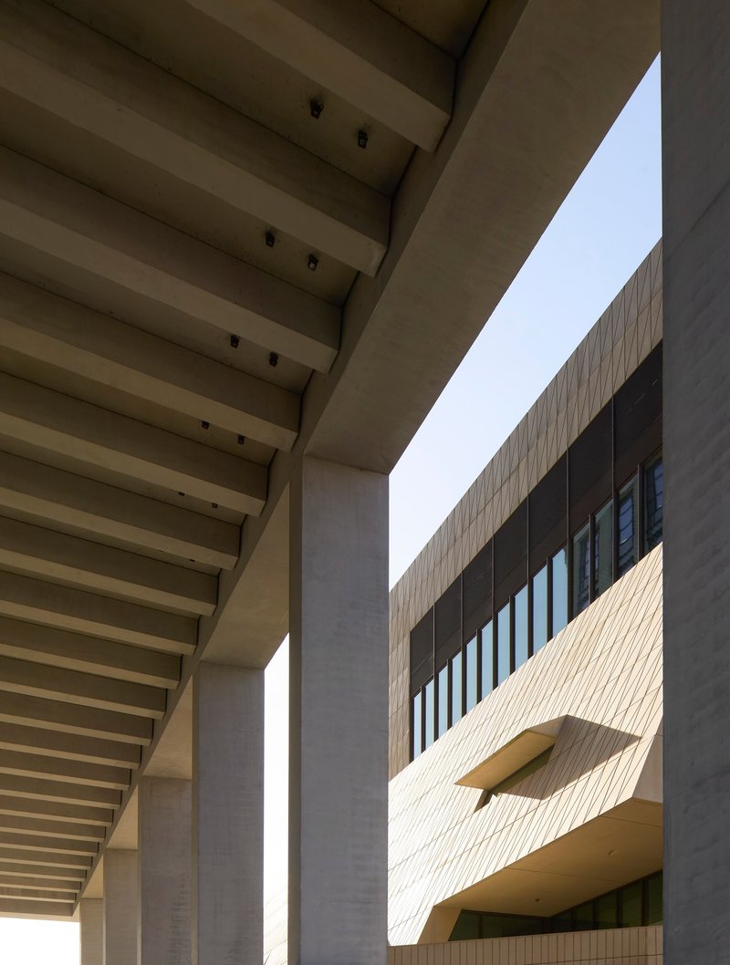 Courtyard view framed by ribbed concrete canopy and facade with angular protruding window opening