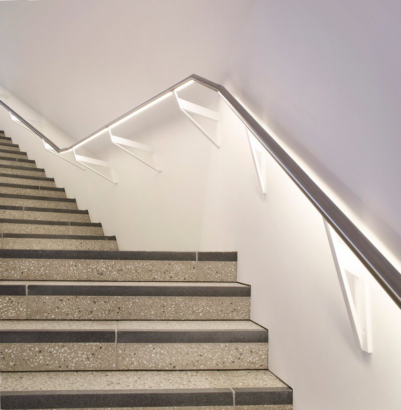 Close-up of the folded metal handrail with integrated LED strip along the terrazzo stair flights