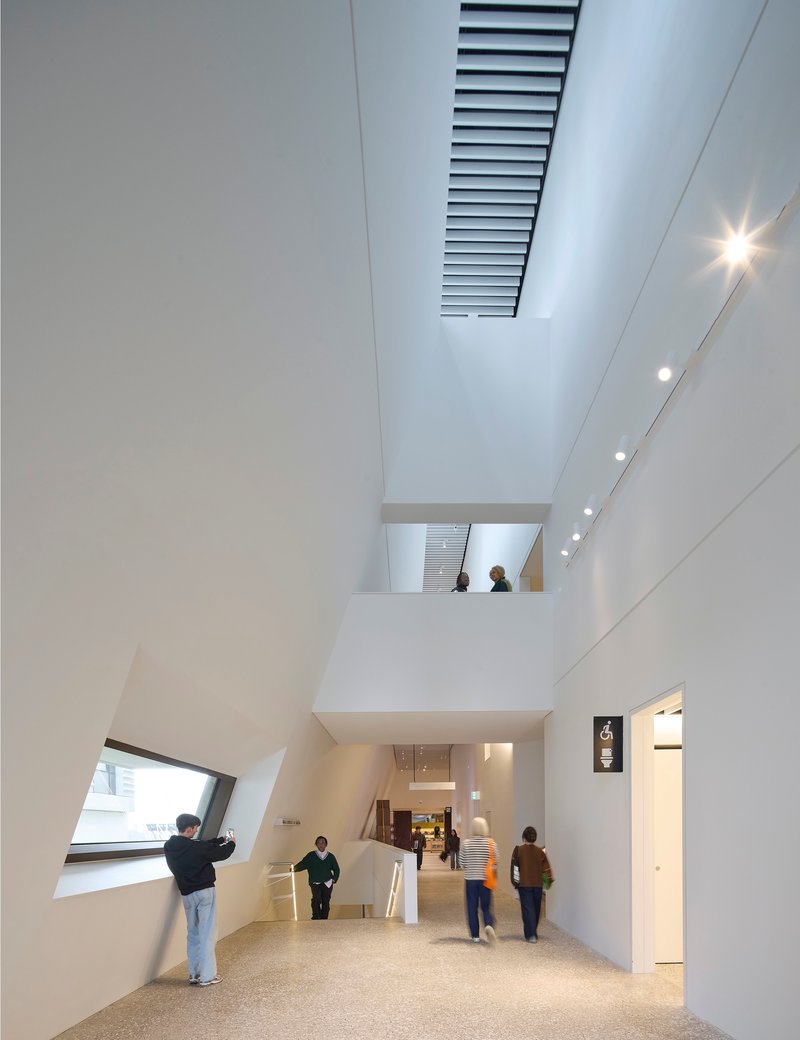 Double-height atrium with angled window, internal balcony and visitors moving through the terrazzo-floored circulation space