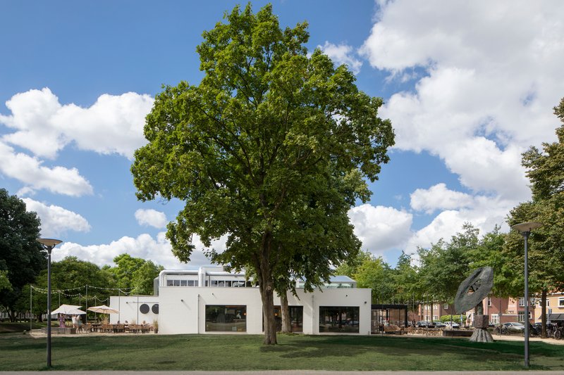 White pavilion with porthole windows and clerestory glazing set in a lawn beneath a mature oak tree
