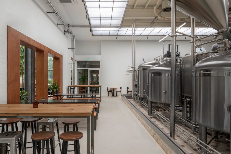 Brewery hall with exposed steel brewing vessels alongside timber-framed doorways and skylights
