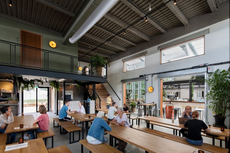 Double-height taproom with mezzanine level and patrons gathered at communal timber benches