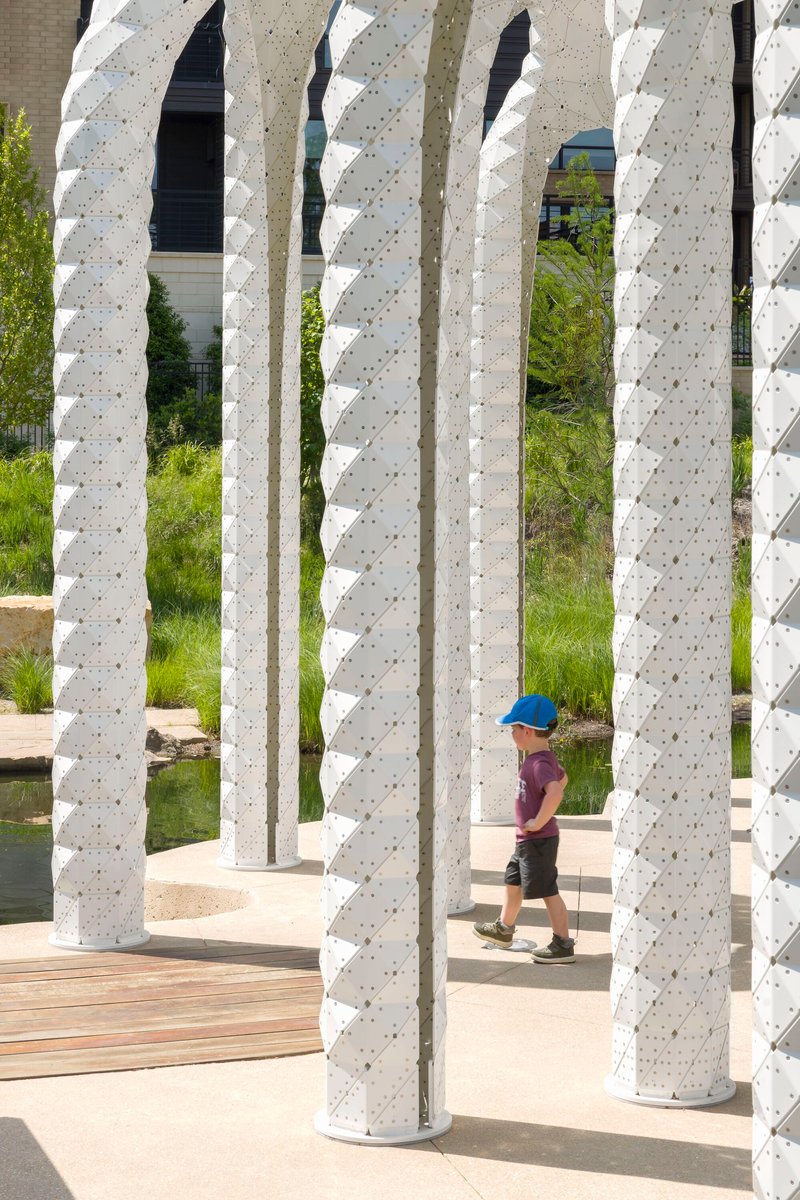 Close view through textured white columns with child in blue cap walking on timber decking