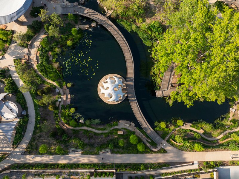 Drone view of circular pavilion in pond surrounded by curving boardwalks and landscape planting