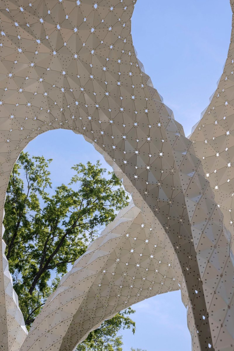 Close-up of the perforated shell structure showing the tiled surface pattern with trees visible beyond