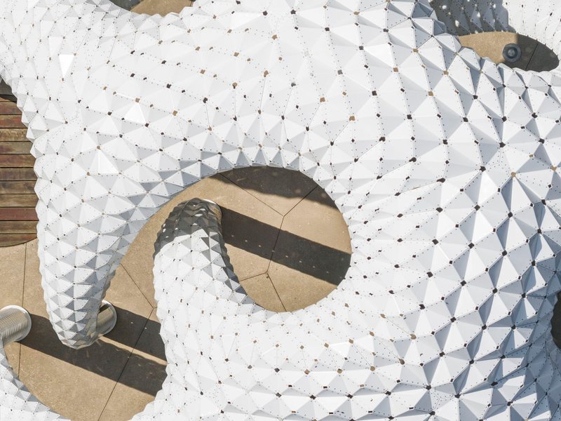 Aerial view of white faceted panels forming circular openings with people casting shadows below