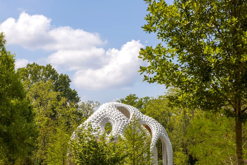 White sculptural loops rising above tree canopy on a partly cloudy summer day