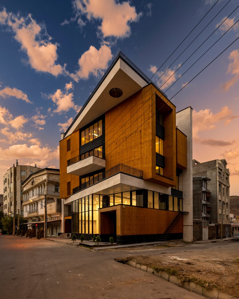 Corner view at sunset showing the angled timber-clad facade and projecting white balconies