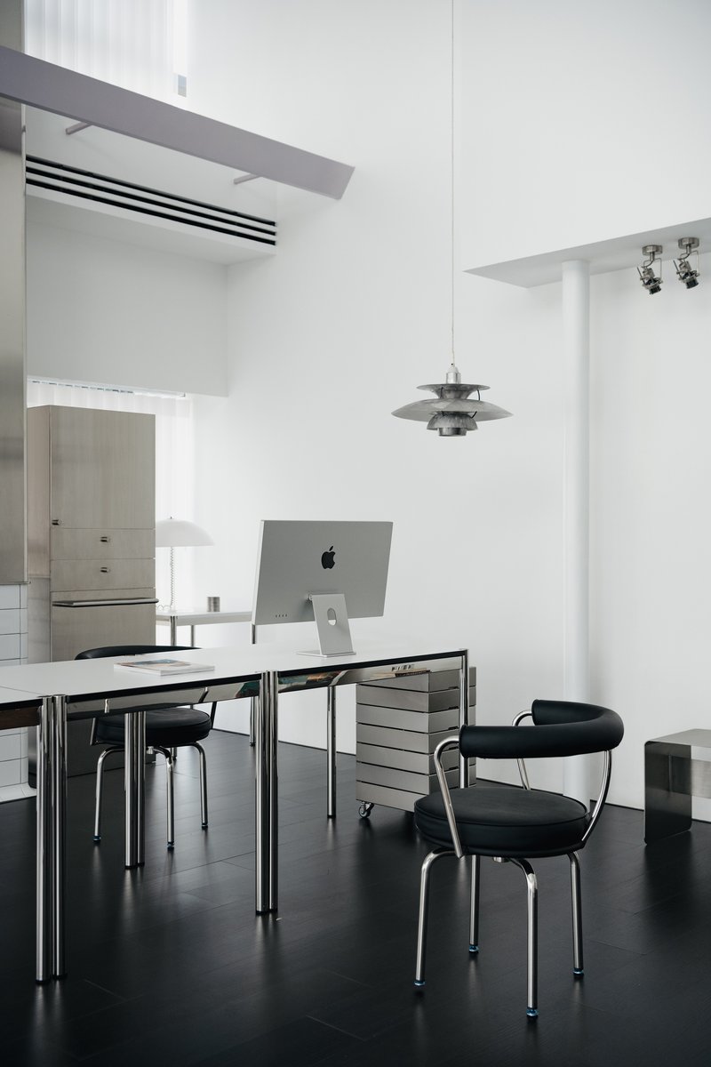 Work table with computer monitor and black chairs beneath a tiered metal pendant in white interior