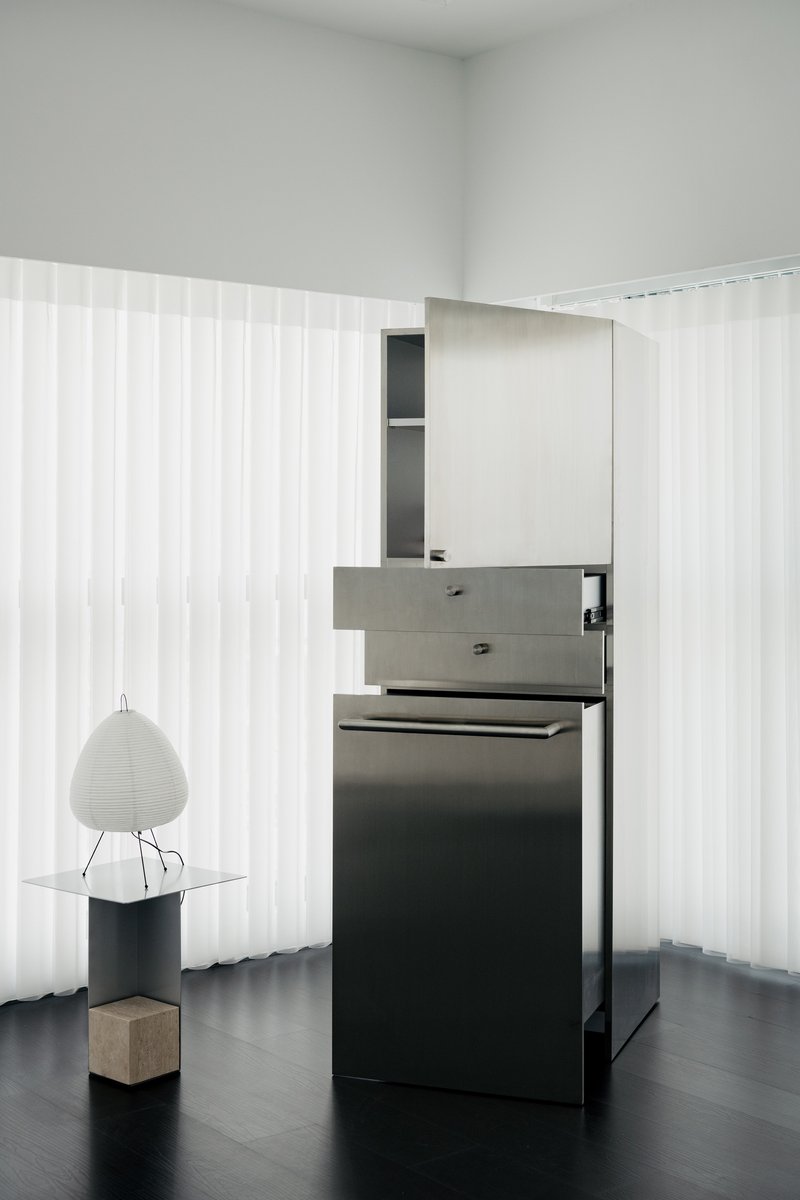 Freestanding kitchen counter with grey drawers and black cabinetry against translucent corrugated wall panels