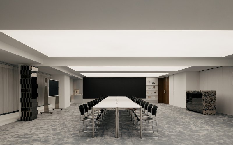 Conference room with long white table beneath continuous skylight and textured column wrapped in dark tiles