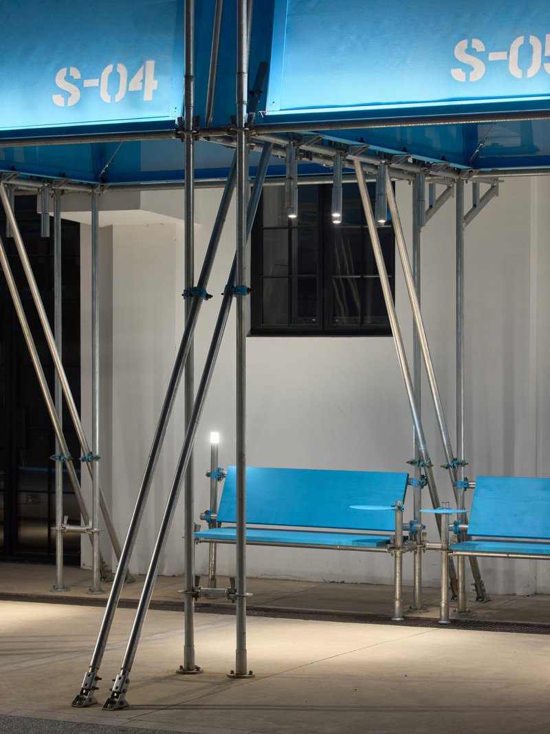 Steel scaffolding swing structure in front of blue and white modular units at dusk