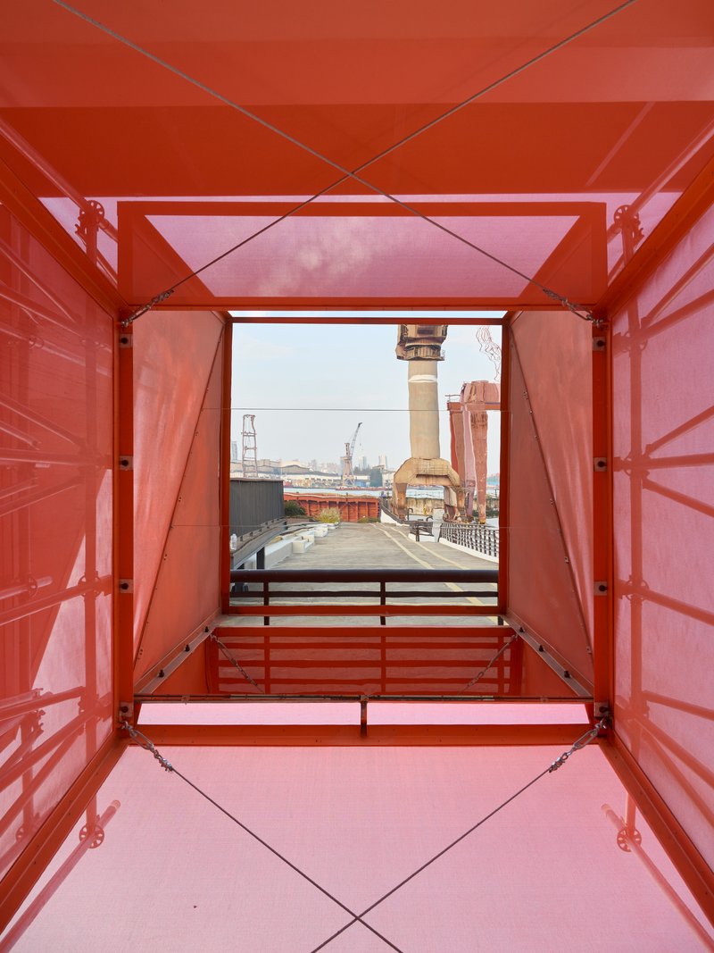 View through orange metal container frame toward shipyard crane and industrial waterfront