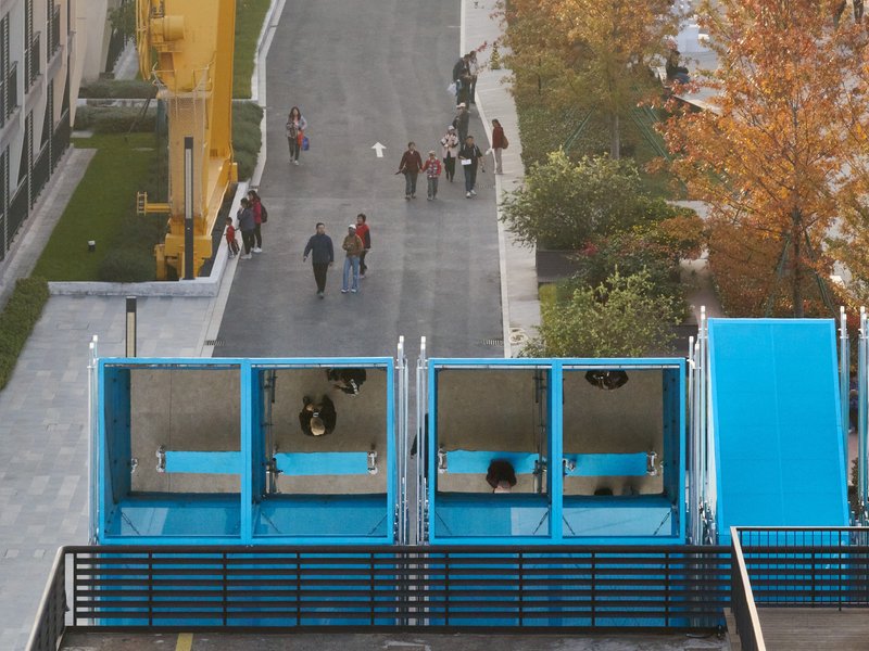 Overhead view of blue pavilion modules with people walking through the plaza and autumn trees nearby