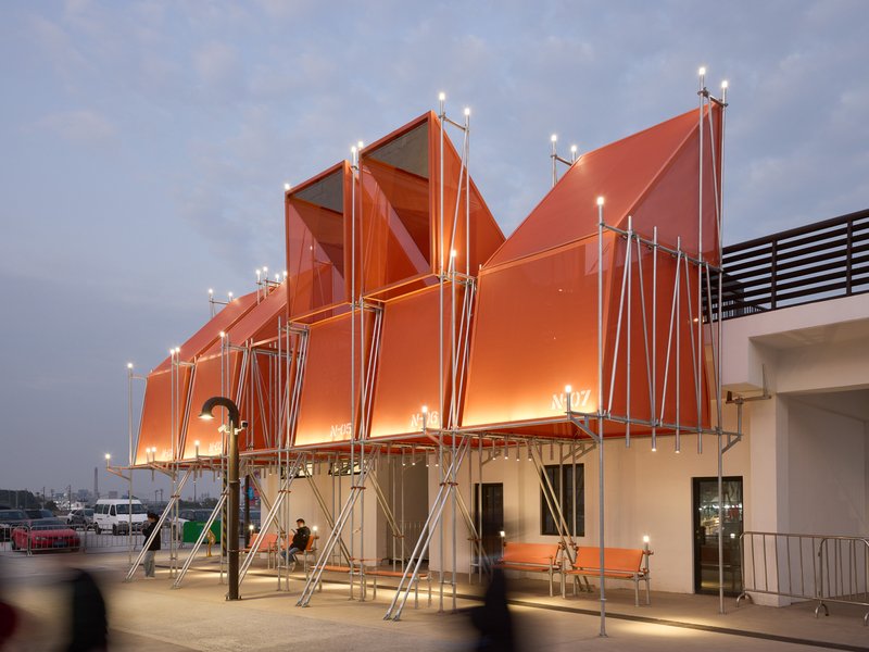 Sawtooth orange canopy with steel pole supports over a plaza at dusk