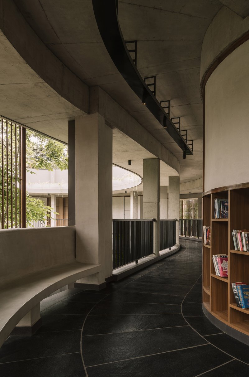 Interior corridor with exposed concrete ceiling beams and curved black tile floor alongside timber bookshelves