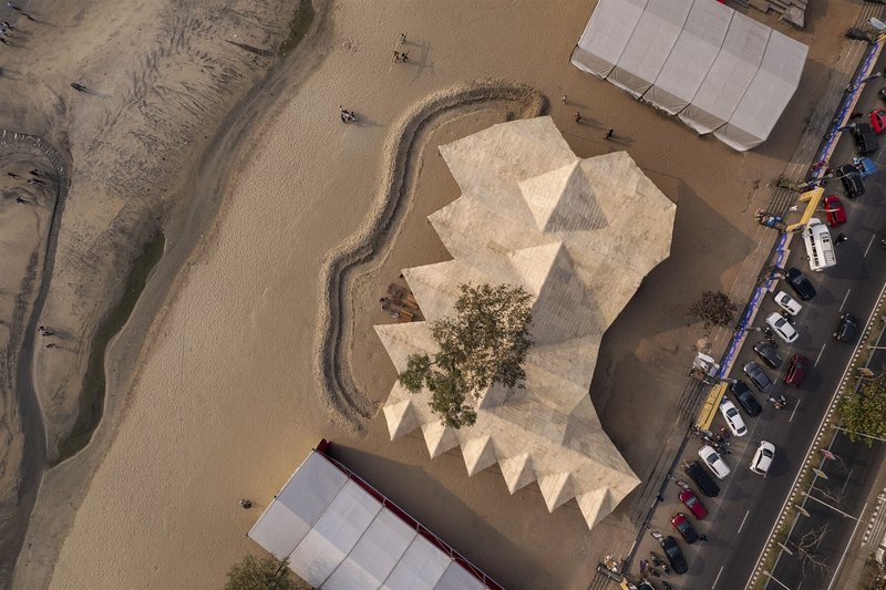 Aerial view of the zigzag woven roof surrounding a tree in a sandy compound