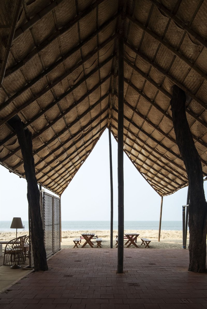 Interior view through a thatched pavilion with timber columns framing the ocean beyond