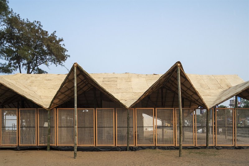 Timber post and mesh panel facade beneath the undulating woven roof in daylight