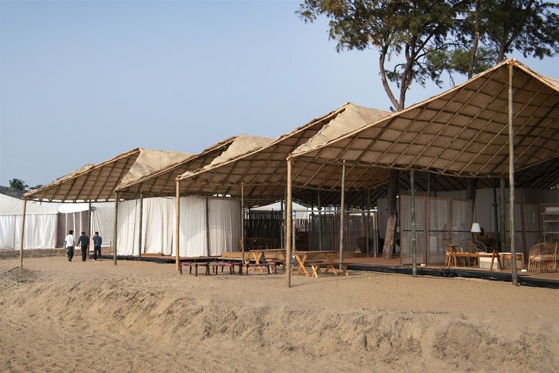 Side elevation showing fabric curtains and timber benches on sand below repeating peaked roof forms