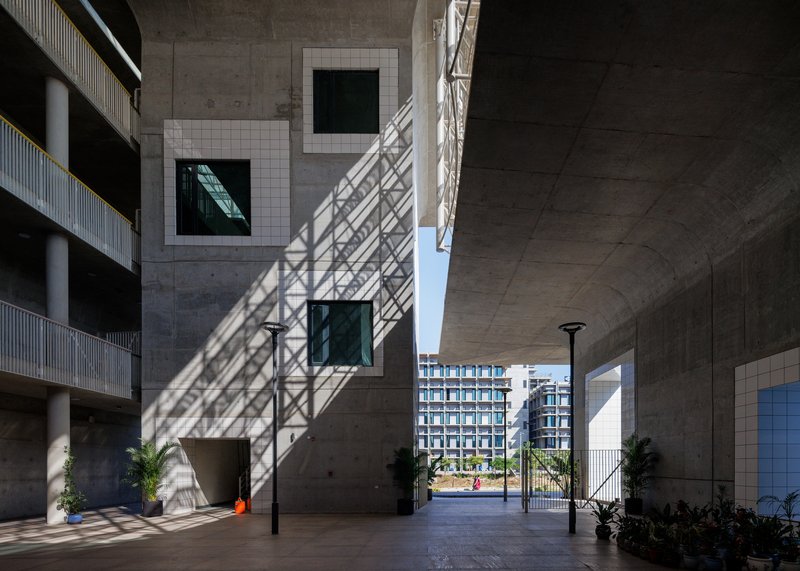 Covered passageway showing diagonal lattice shadows across concrete walls and potted plants near the entrance