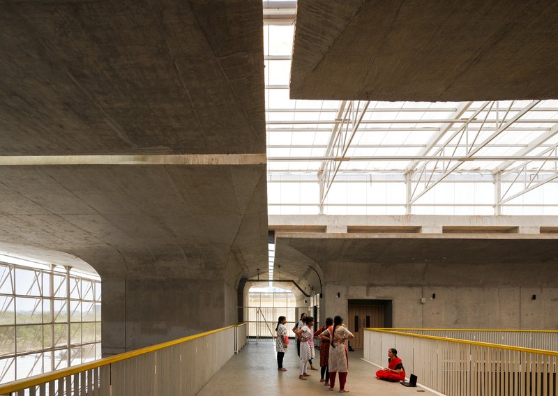 Upper level corridor with yellow metal railing overlooking the atrium under a steel truss roof