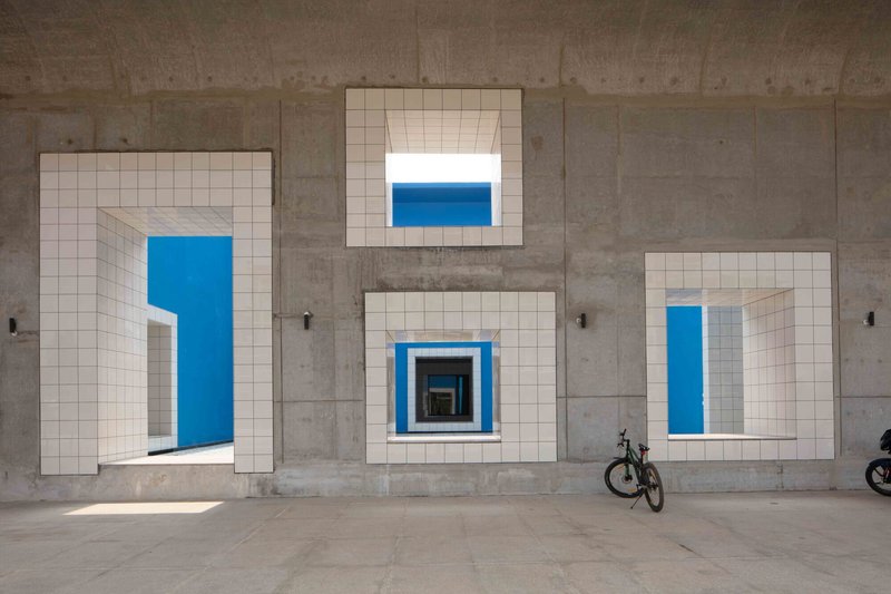 Facade detail showing four white tile-framed openings set into the board-formed concrete wall with a bicycle below