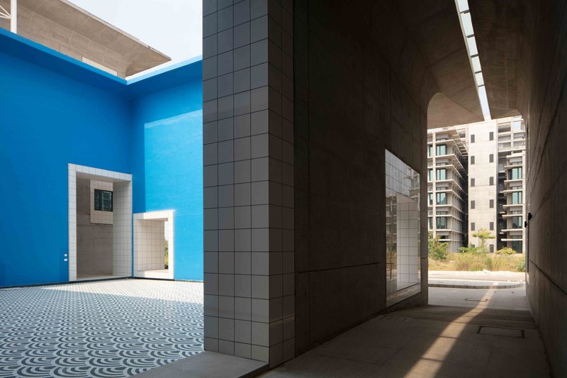 Covered walkway looking toward a blue-painted courtyard framed by white tile columns and concrete ceiling slot