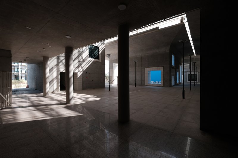 Interior ground floor with polished concrete columns casting diagonal shadows across the floor from clerestory light above