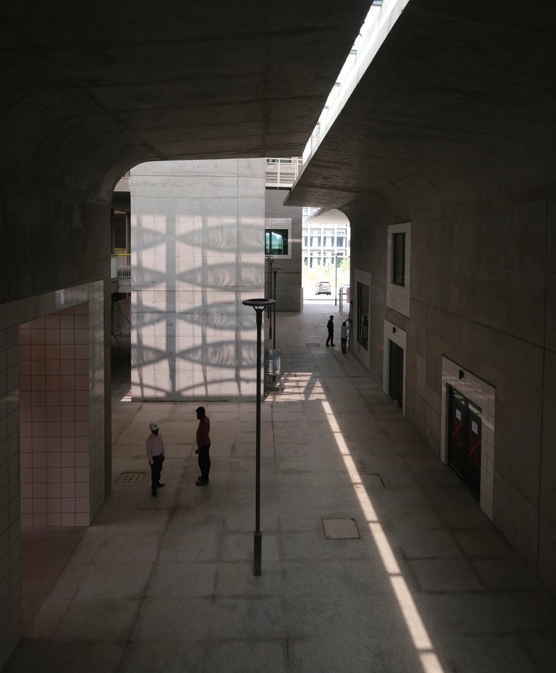 Interior street with translucent screen wall and shaft of sunlight casting shadows on concrete pavement