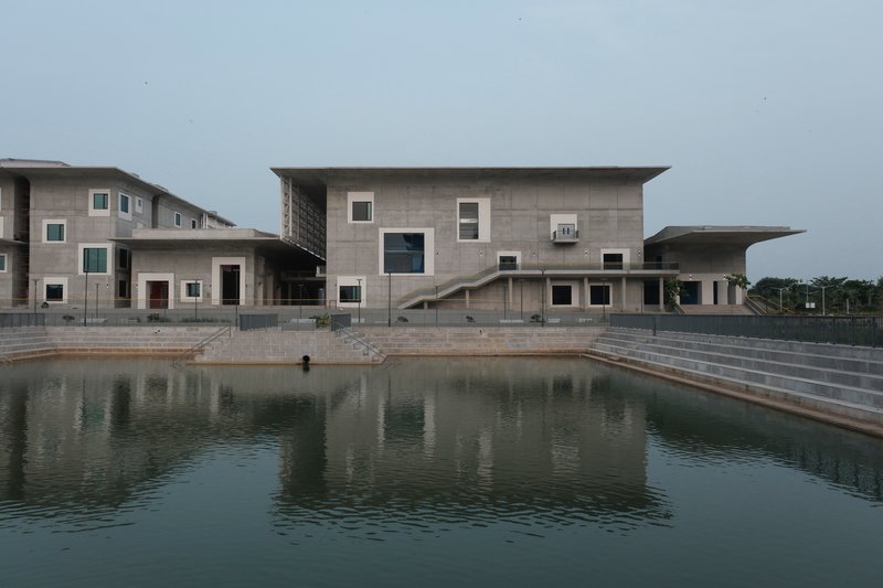 Concrete facade with scattered square windows reflected in a still pond under overcast sky