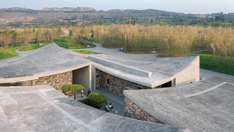 Aerial view of angular concrete roof planes punctured by a courtyard over stone masonry walls in autumn
