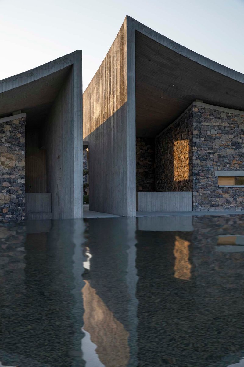 Covered entry passage with board-formed concrete columns and shallow reflecting pool catching late afternoon light
