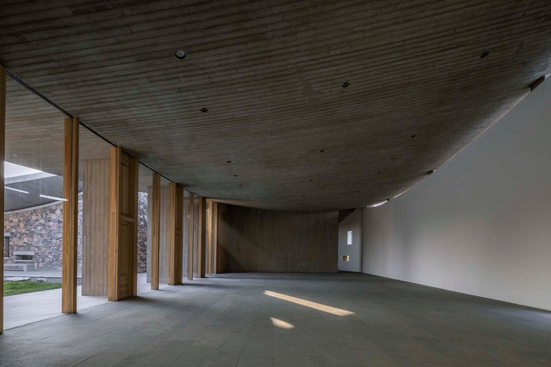 Gallery space with angled timber ceiling and timber columns opening to a courtyard