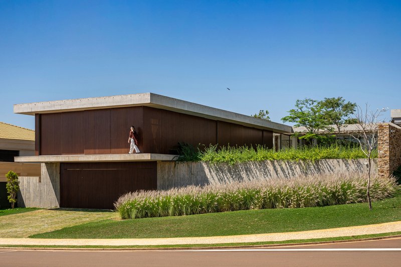 Street view of the dark timber-clad upper volume with concrete soffit above planted grasses and lawn