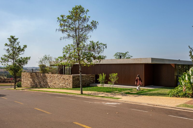 Stone perimeter wall and dark timber facade from the street with scattered trees under clear sky