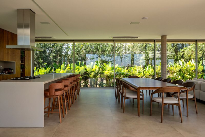 Dining area with kitchen island and glass wall overlooking planted bed of large-leafed tropical vegetation