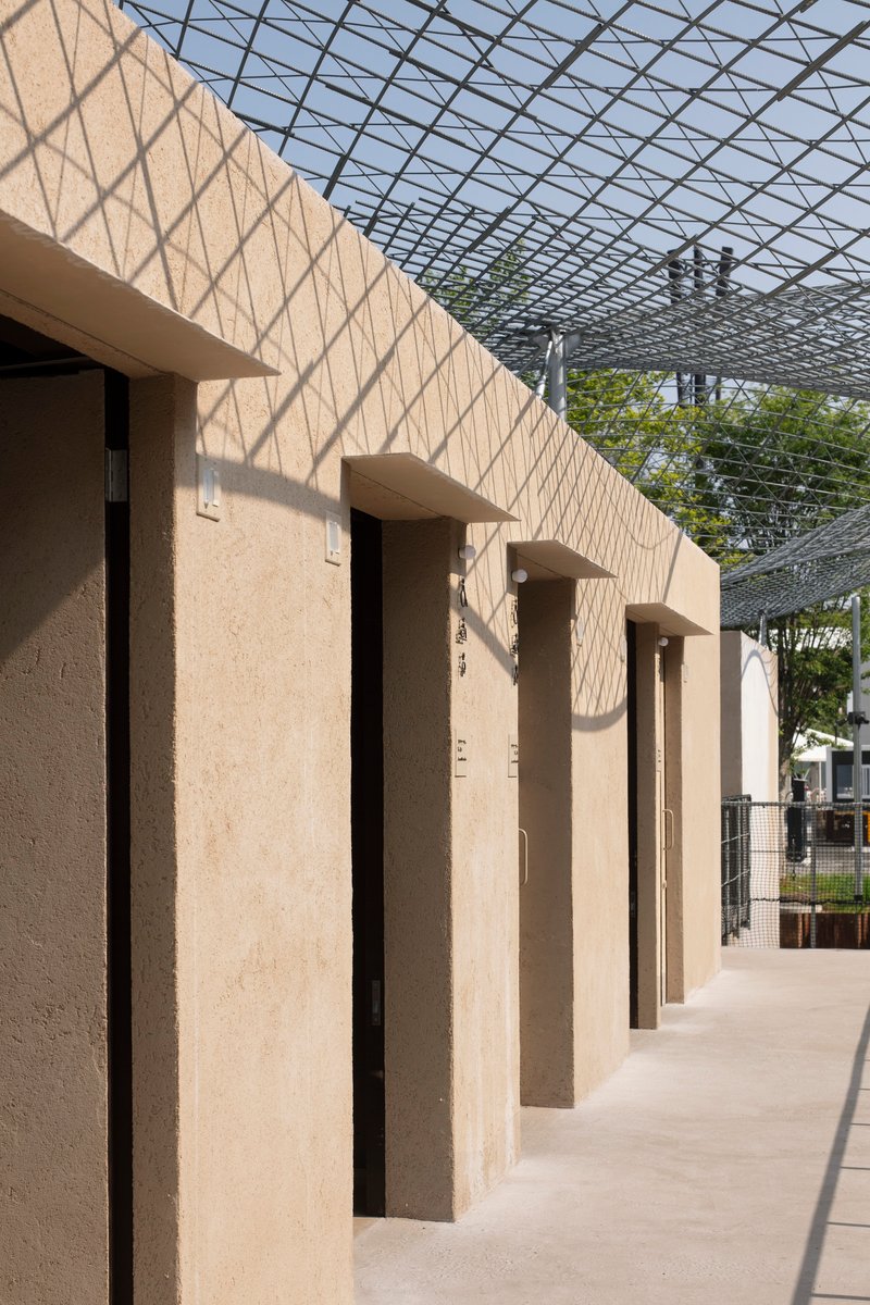Row of vertical recesses in the rammed earth facade creating rhythmic shadows under the canopy