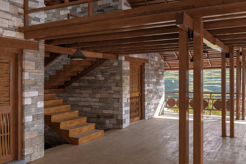 Cantilevered timber staircase rising between stone walls with exposed beam ceiling and columns throughout the space