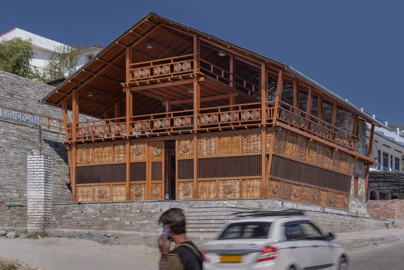 Street view of the timber frame facade with woven panels and stone base beneath a clear blue sky