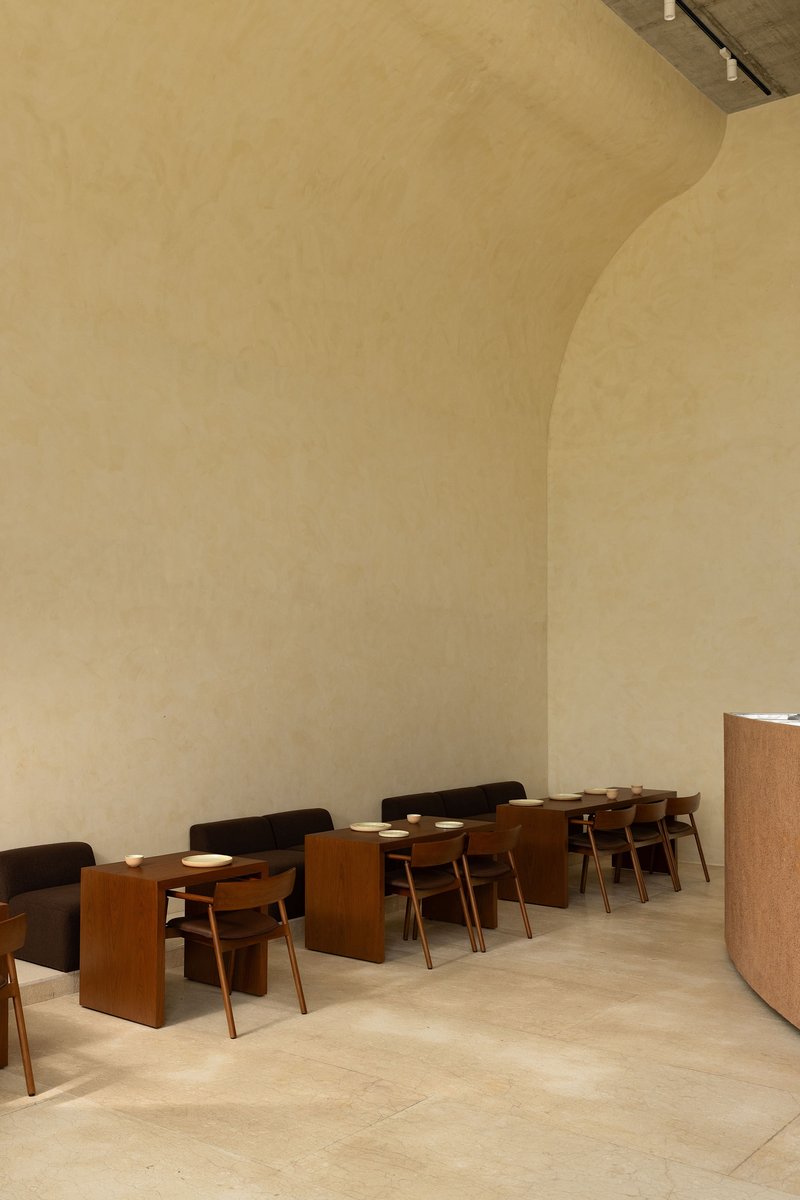 Row of timber dining tables and chairs beneath a curved plaster ceiling in soft light