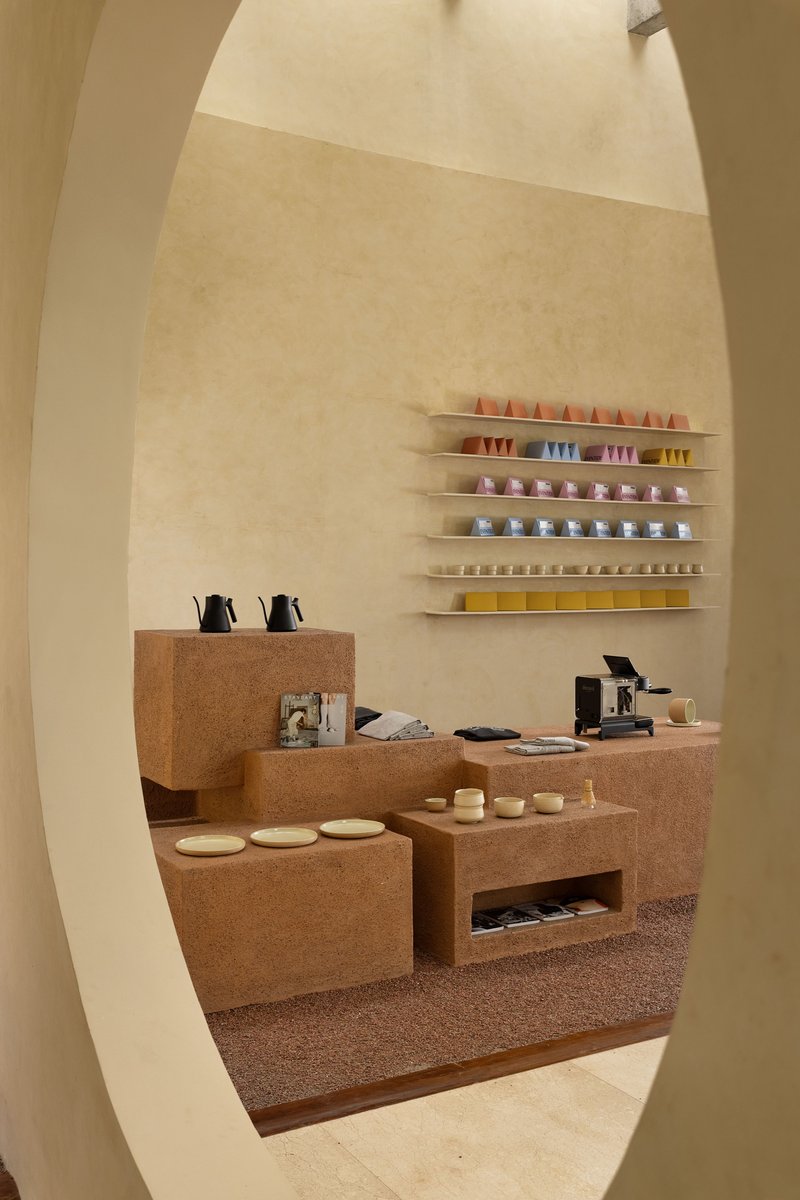 View through curved opening to coffee counter with cork surfaces and colorful cups on wall shelves