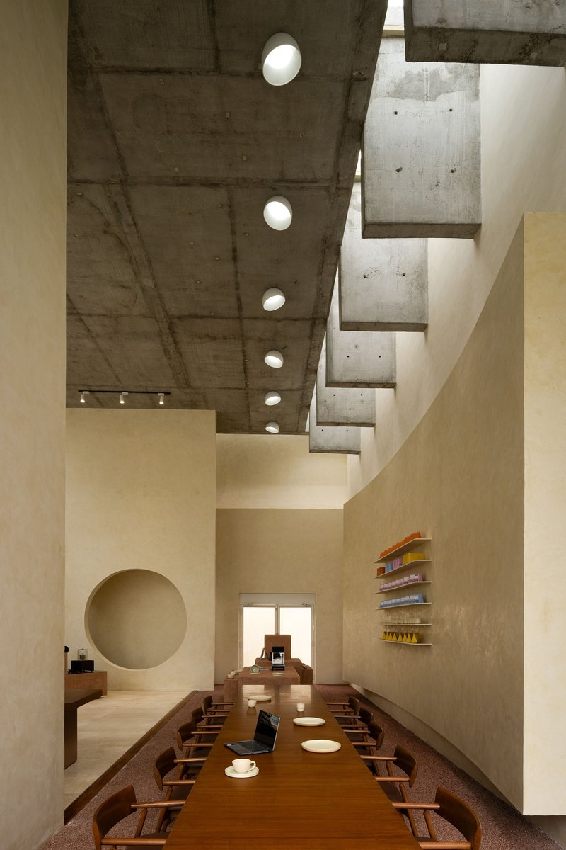 Double-height dining space with exposed concrete ceiling, circular skylights and a long communal table
