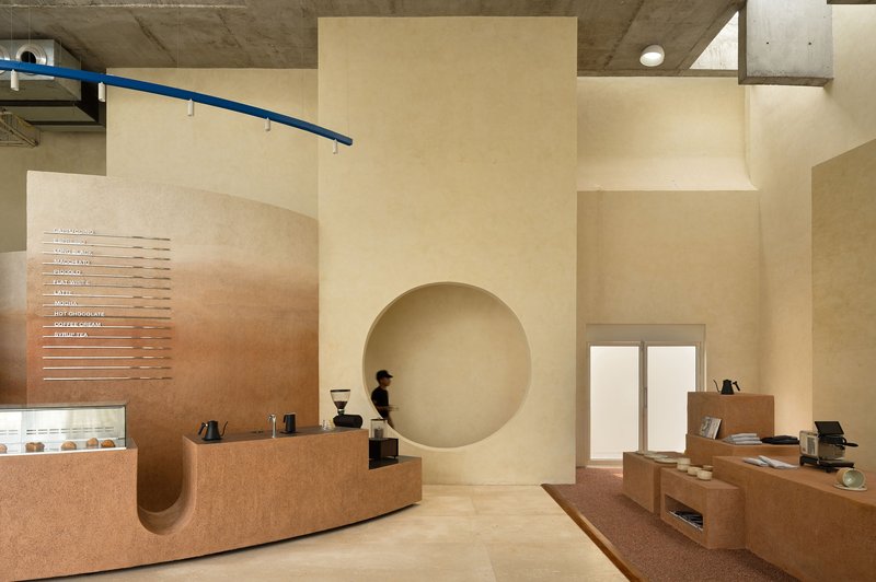 Interior of a cafe with curved cork service counter and circular wall niche under exposed concrete ceiling