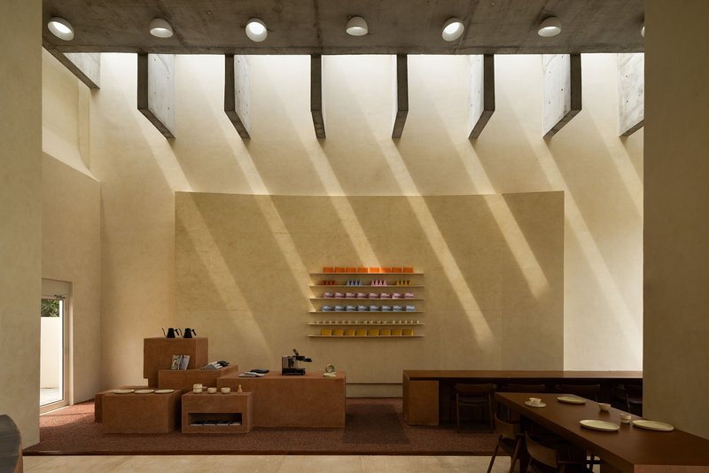 Interior wall with timber shelving and cork display tables illuminated by diagonal shadows from overhead skylights