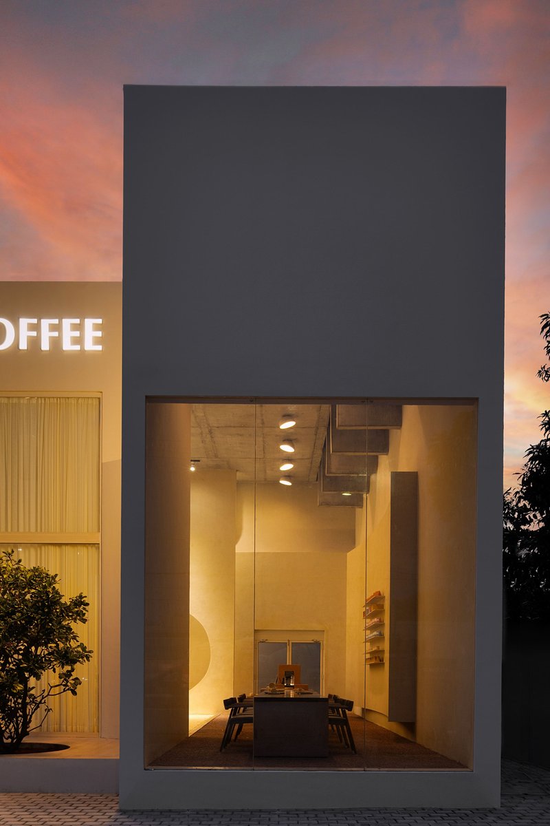 Tall glazed opening framing an illuminated staircase and table at dusk with pink sky